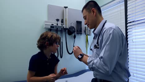 Side-view-of-young-asian-male-doctor-applying-band-aid-on-caucasian-boy-patient-arm-in-clinic-4k
