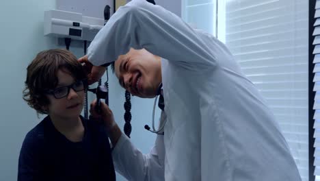 Side-view-of-young-asian-male-doctor-examining-a-caucasian-boy-patient-ear-with-tool-in-a-clinic-4k