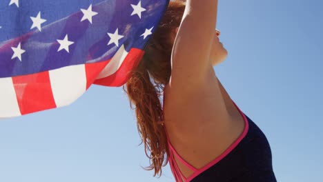 Mujer-Parada-Junto-Al-Mar-Con-Una-Bandera-Americana-Ondeando.-En-La-Playa-4k