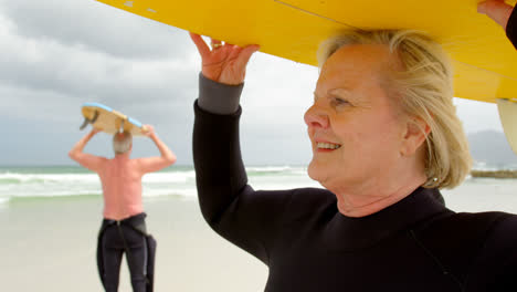 Close-up-of-old-caucasian-woman-carrying-surfboard-on-her-head-at-beach-4k