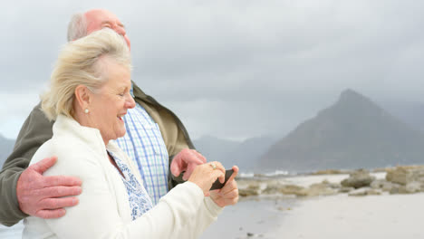 Side-view-of-old-caucasian-senior-couple-taking-selfie-with-mobile-phone-at-beach-4k