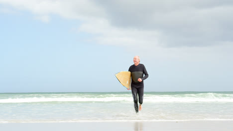Front-view-of-old-caucasian-senior-man-running-with-surfboard-at-beach-4k