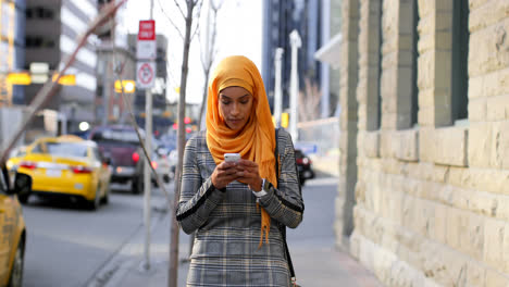 Vista-Frontal-De-Una-Joven-Asiática-Con-Hijab-Usando-Un-Teléfono-Móvil-En-La-Ciudad-4k