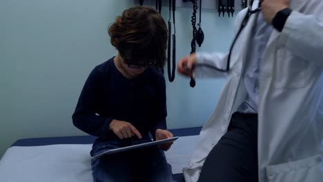 Side-view-of-young-asian-male-doctor-examining-caucasian-boy-patient-in-a-clinic-4k