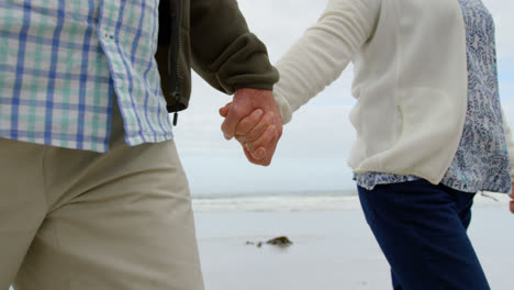 Mid-section-of-old-caucasian-couple-walking-hand-in-hand-at-beach-4k