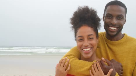 Vorderansicht-Eines-Jungen-Schwarzen-Paares,-Das-Sich-Umarmt-Und-Am-Strand-In-Die-Kamera-Blickt,-4k