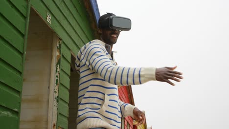 Side-view-of-young-black-man-gesturing-while-using-virtual-reality-headset-at-beach-hut-4k