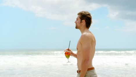 Seitenansicht-Eines-Jungen-Kaukasischen-Mannes,-Der-Mit-Cocktail-Am-Strand-Spaziert,-4k