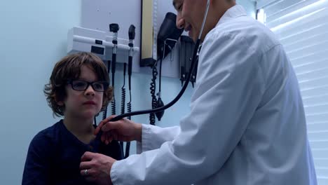 Side-view-of-young-asian-male-doctor-examining-caucasian-boy-patient-chest-in-a-clinic-4k