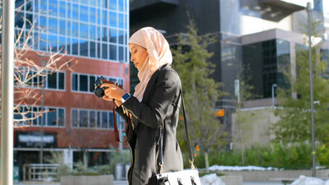 Vista-Lateral-De-Una-Joven-Asiática-Con-Hijab-Haciendo-Clic-En-Fotos-Con-Cámara-Digital-En-La-Ciudad-4k
