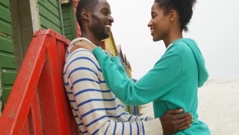 Side-view-of-young-romantic-black-couple-embracing-and-standing-at-beach-hut-on-a-sunny-day-4k