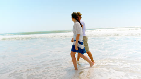 Side-view-of-young-caucasian-couple-walking-with-hand-in-hand-at-beach-4k
