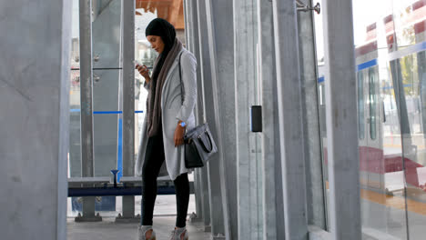 Side-view-of-young-Asian-woman-in-hijab-using-mobile-phone-at-railway-station-4k