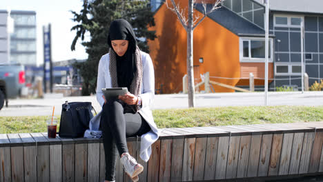 Vista-Frontal-De-Una-Joven-Asiática-Con-Hijab-Usando-Una-Tableta-Digital-En-La-Ciudad-4k