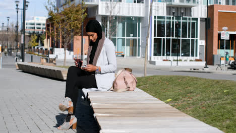 Seitenansicht-Einer-Jungen-Asiatischen-Frau-Im-Hijab,-Die-In-Der-Stadt-Ihr-Mobiltelefon-Benutzt,-4K