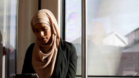 Vista-Frontal-De-Una-Joven-Asiática-Con-Hijab-Usando-Una-Tableta-Digital-Y-Viajando-En-Tren-4k