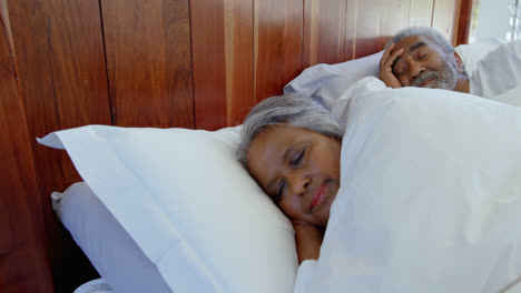 Side-view-of-mixed-race-senior-couple-sleeping-in-bedroom-at-home-4k