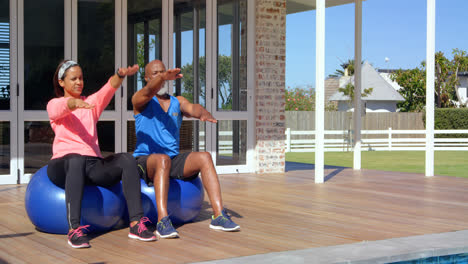 Mixed-race-mature-couple-exercising-together-on-exercise-ball--at-backyard-on-a-sunny-day-4k