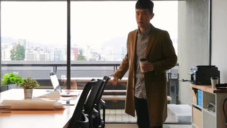 Front-view-of-young-Asian-businessman-walking-with-coffee-cup-in-modern-office-4k
