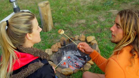 Young-man-feeding-woman-with-marshmallow-near-campfire-4k