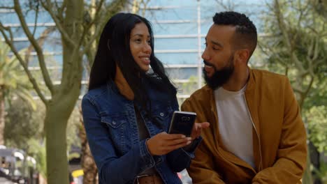Front-view-of-young-mixed-race-couple-discussing-over-mobile-phone-in-the-city-4k