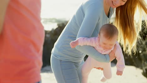 Side-view-of-mid-adult-caucasian-mother-playing-with-baby-at-beach-on-a-sunny-day-4k