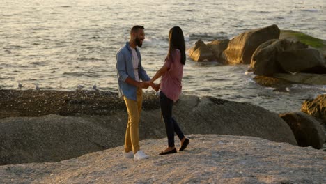 mixed-race-Couple-holding-hands-while-standing-on-rock-at-beach-4k
