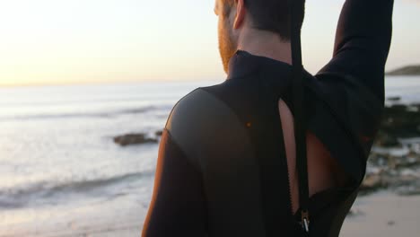 Rückansicht-Eines-Kaukasischen-Mannes-Mittleren-Alters-Im-Surfanzug-Am-Strand-Bei-Sonnenuntergang-4k