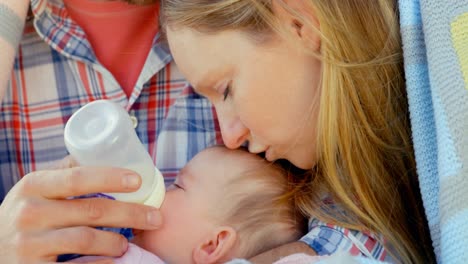 Close-up-of-mid-adult-caucasian-parents-feeding-their-baby-from-a-bottle-on-a-sunny-day-4k