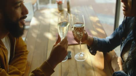 Side-view-of-young-mixed-race-couple-toasting-wine-glasses-in-cafe-4k