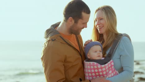 Front-view-of-mid-adult-caucasian-parents-looking-at-baby-at-beach-on-a-sunny-day-4k
