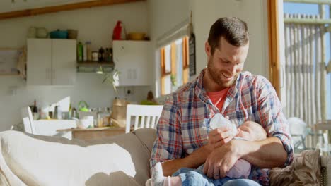 Front-view-of-mid-adult-caucasian-father-feeding-milk-his-baby-from-bottle-in-a-comfortable-home-4k