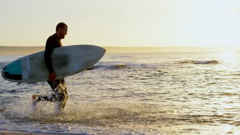 Side-view-of-mid-adult-caucasian-male-surfer-with-surfboard-running-in-sea-during-sunset-4k