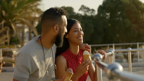 Happy-mixed-race-couple-standing-with-ice-cream-cones-at-promenade-4k