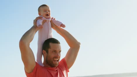 Front-view-of-mid-adult-caucasian-father-carrying-baby-on-shoulder-on-a-sunny-day-4k