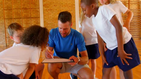 Sports-teacher-and-schoolkids-discussing-over-clipboard-in-the-basketball-court-4k