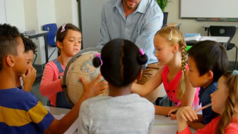 Caucasian-male-teacher-teaching-his-kids-about-globe-in-classroom-4k