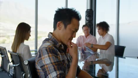 Thoughtful-young-Asian-male-executive-sitting-at-table-in-conference-room-in-office-4k