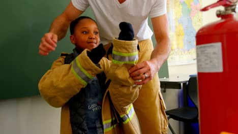 Männlicher-Feuerwehrmann-Hilft-Afroamerikanischem-Mädchen,-Im-Klassenzimmer-Feuerwehruniform-Zu-Tragen.-Schulmädchen-Lächelt