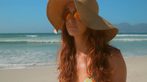 Beautiful-young-Caucasian-woman-in-bikini-with-sunglasses-and-hat-standing-on-beach-4k