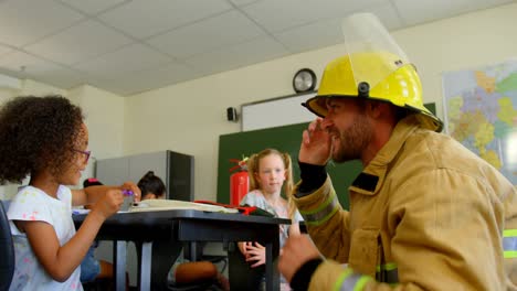 Young-Caucasian-male-firefighter-teaching-schoolgirl-about-fire-safety-in-classroom-4k