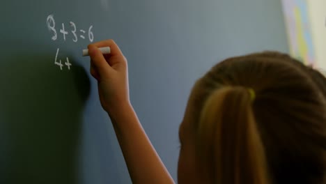 Schoolgirl-writing-on-chalkboard-with-chalk-in-classroom-at-school-4k