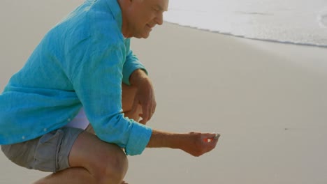 Side-view-of-active-senior-Caucasian-man-holding-a-seashell-on-the-beach-4k