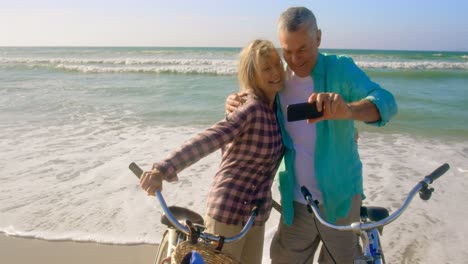 Vorderansicht-Eines-Aktiven-älteren-Kaukasischen-Paares,-Das-Am-Strand-Ein-Selfie-Mit-Dem-Mobiltelefon-Macht,-4k