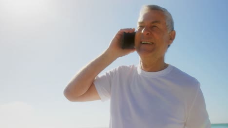 Front-view-of-active-senior-Caucasian-man-talking-on-mobile-phone-at-beach-4k