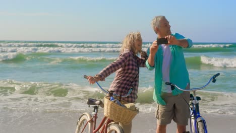 Vorderansicht-Eines-Aktiven-älteren-Kaukasischen-Paares,-Das-Am-Strand-Ein-Selfie-Mit-Dem-Mobiltelefon-Macht,-4k