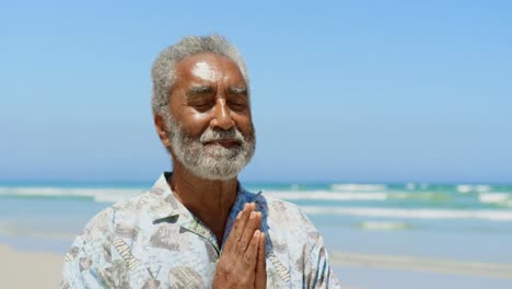 Vista-Frontal-De-Un-Hombre-Afroamericano-Senior-Activo-Realizando-Yoga-En-La-Playa-4k