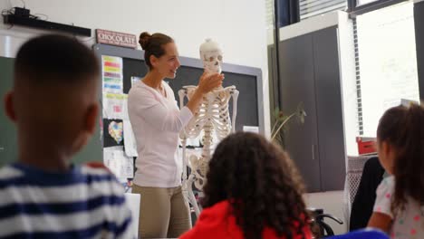 Vista-Frontal-De-Una-Profesora-Caucásica-Explicando-El-Modelo-De-Esqueleto-Humano-En-El-Aula-4k