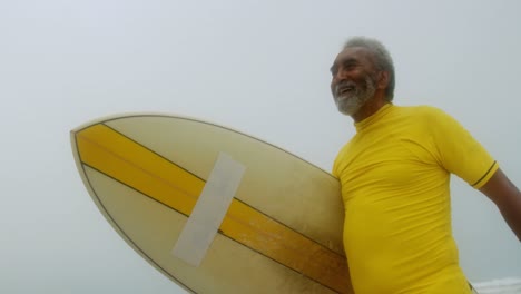 Low-angle-view-of-active-senior-African-American-man-with-surfboard-walking-on-the-beach-4k