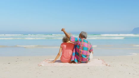 Rear-view-of-active-senior-African-American-couple-relaxing-on-blanket-in-the-sunshine-at-beach-4k